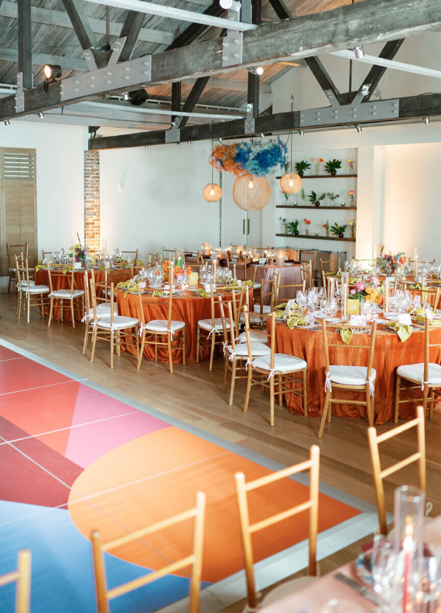 Orange velvet tablecloths on round tables were arranged on one side of the colorful dance floor at an art-inspired wedding reception.