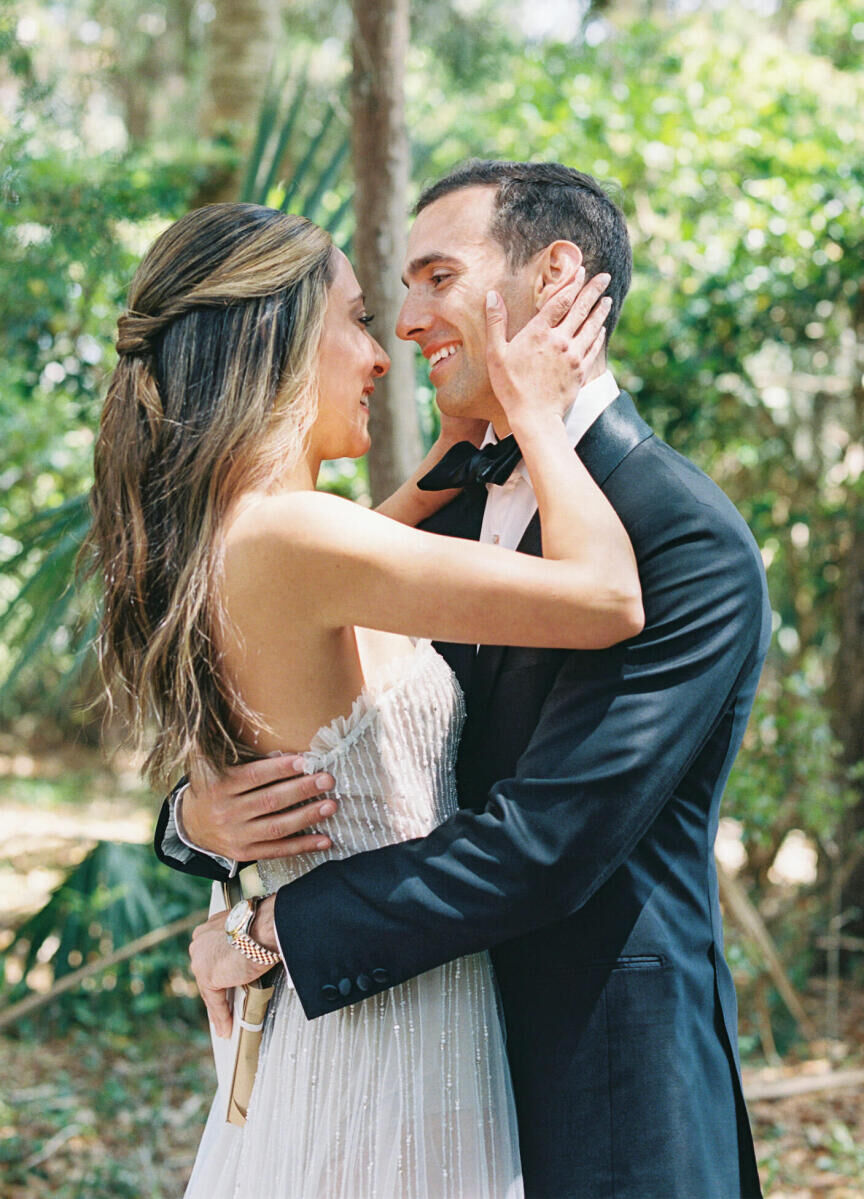 A bride wearing a knotted half-up hairstyle grabs her husband's face while he embraces her at their elegant spring wedding.