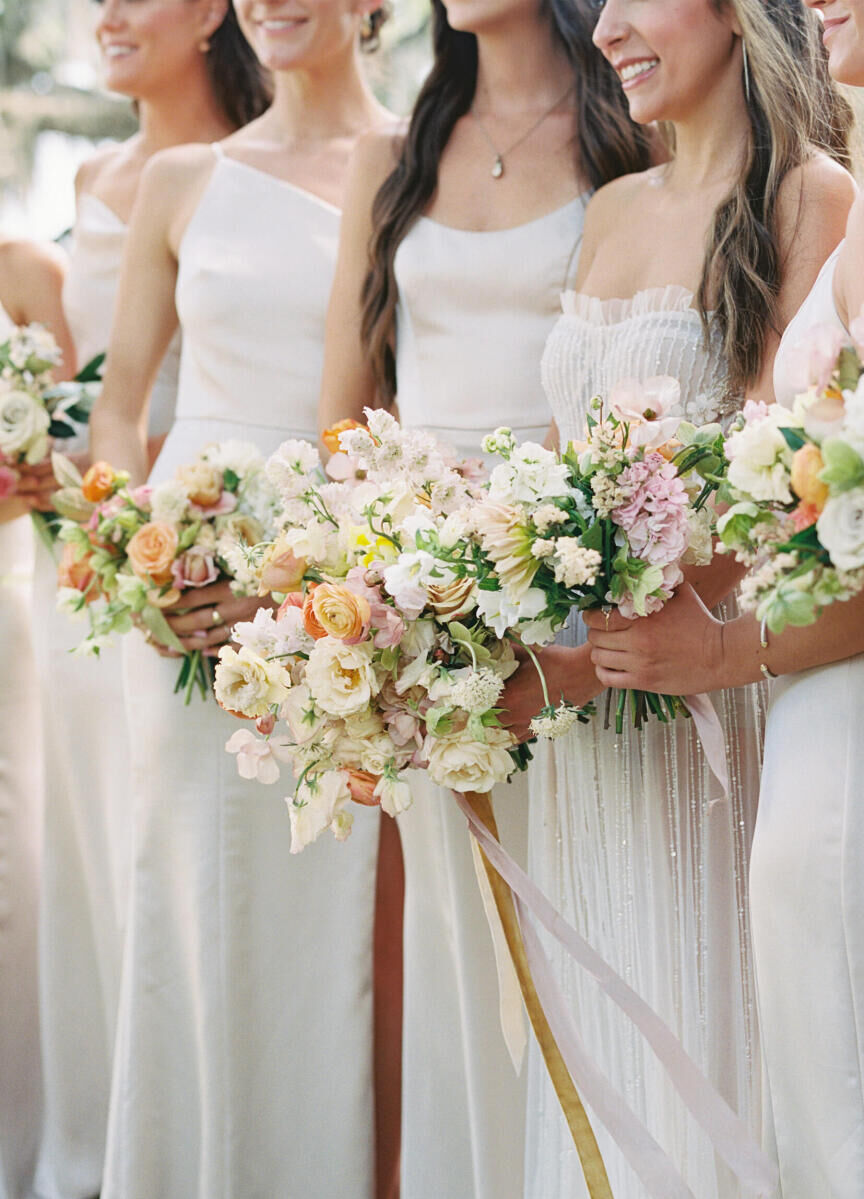 A bride and her bridesmaids hold cheerful bouquets of soft pastel blooms during her elegant spring wedding.