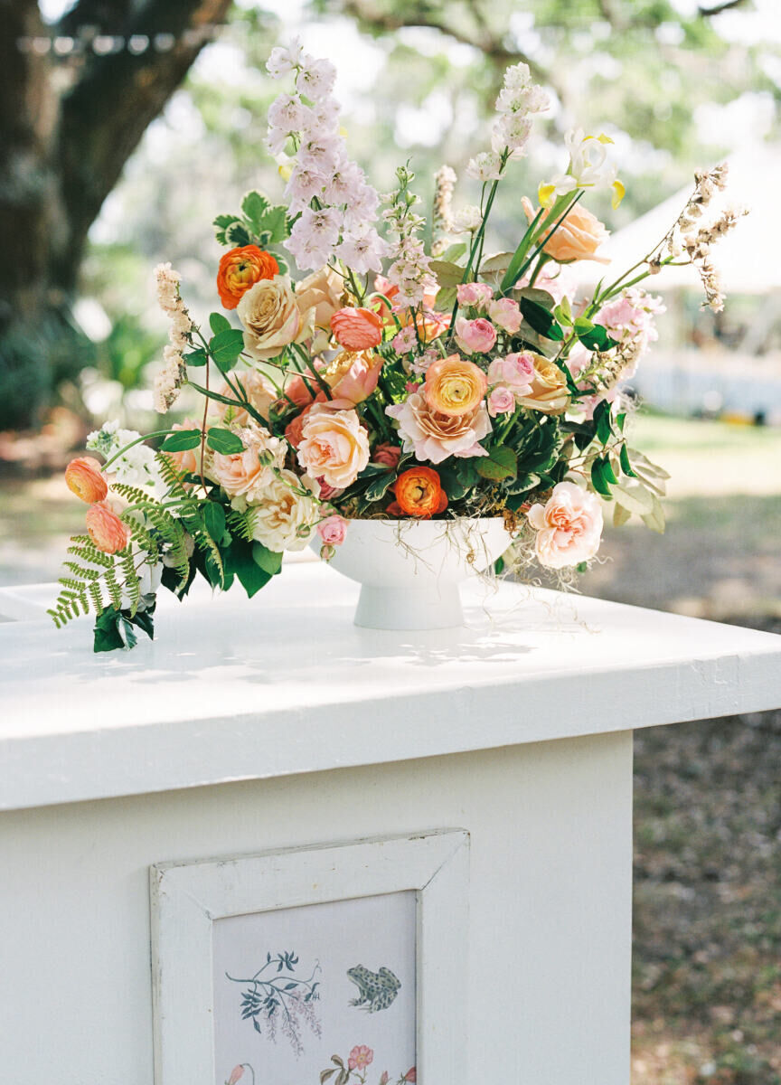 A floral arrangement accenting a bar at an elegant spring wedding featured ranunculus, roses, and an assortment of other blooms and greenery to give it an organic shape and feel.