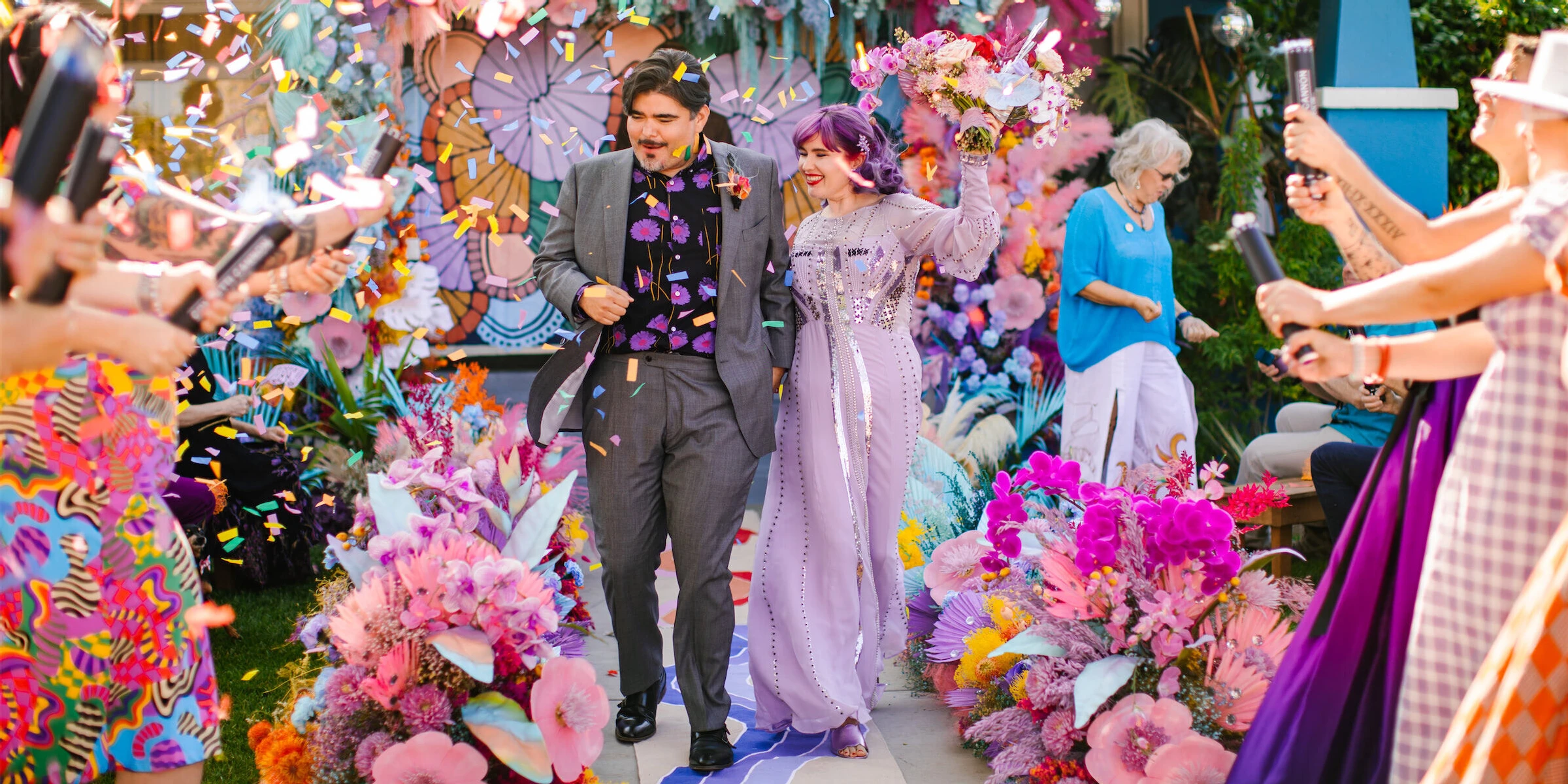 A happy couple recesses up their flower-flanked aisle amidst a shower of biodegradable confetti at the end of their vibrant, outdoor wedding ceremony.